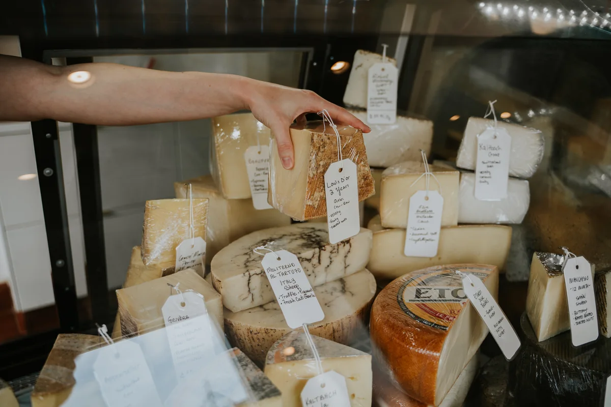 A hand selecting artisan cheese from a local shop counter